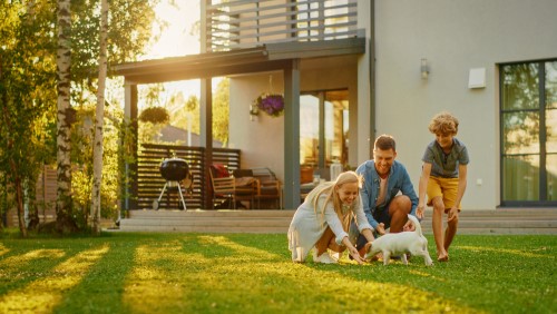 Family playing with a puppy in the yard in front of an insured home